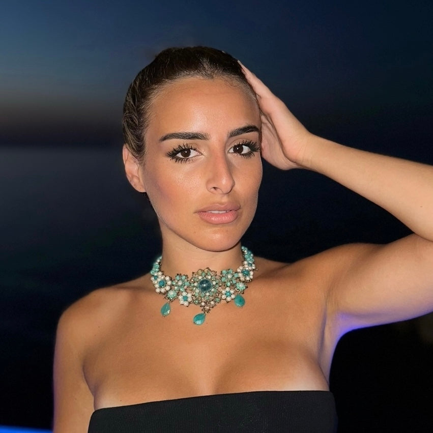 Modella indossa una collana girocollo elegante con dettagli in pietre colorate, sotto il cielo notturno.